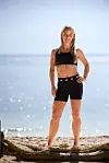 Kvinde i sort Adidas-træningstøj står på en solrig strand ved havet