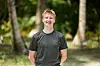 Ung mand i mørk T-shirt smiler foran palmer i en tropisk skov