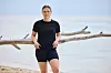 Person i sort sportstøj læner sig mod drivtømmer på en sandstrand ved havet.