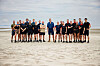 Gruppe af personer i sportstøj står på sandstrand og kigger mod kameraet
