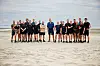 Gruppe af personer i sportstøj står på sandstrand og kigger mod kameraet