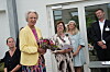 Gruppe mennesker ved Strax-arrangement foran glasdør, kvinde holder blomster
