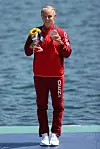 Emma Aastrand Jørgensen i rød dansk træningsdragt holder bronzemedalje og blomster foran vandet.