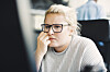 Person med briller ser koncentreret på computerskærm i åbent kontor