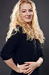 Portræt af lyshåret kvinde med krøllet hår i mørk bluse mod neutral baggrund.