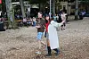 To unge går gennem en festivalplads med træer, bænke og barområde i baggrunden.