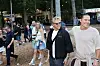Festivalgæster går gennem skovområde med boder og lys i baggrunden.
