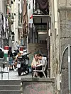 Folk sidder og snakker i en smal trappegade med scootere og vasketøj