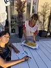 To kvinder ved udendørs bord, én laver frisk pasta med kagerulle