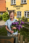 Kvinde med lilla syrener står foran den gule Femø Kro