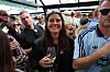 Smilende kvinde med vinglas omgivet af mennesker ved udendørs fest
