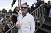 Mand i hvid skjorte med drink står ved trappe omgivet af festivalgæster på Smukfest.