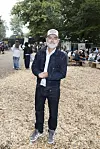 Mand i denim og kasket står på træflis midt blandt gæster på Smuk Festival i skoven.