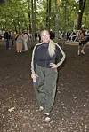 Festivalgæst i sportstøj går på skovsti med lyskæder og publikum i baggrunden.
