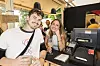 Festivalgæster smiler ved barens kasseområde i et træbygget telt.