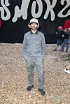 Mand i gråt tøj står på træflis foran sort væg med grafisk tekst på SMUK Festival 2026.