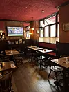 Tom restaurant med træmøbler, røde bænke og tv-skærm med sport på væggen.