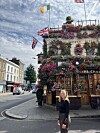 Person foran blomsterpyntet pub med britiske og irske flag på hjørne i by