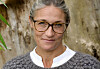 Mia Wagner med briller og gråt strik poserer foran en træstamme.