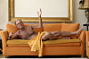 Jan Hertz ligger afslappet på en orange sofa i en stue med stor gylden ramme bag sig.
