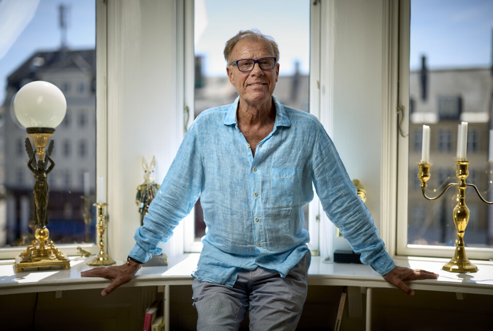 Billede 5 - Jan Hertz ved vindue med messinglamper i et lyst kontor med byudsigt.