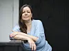 Kvinde i lyseblå bluse læner sig mod gelænder foran sort trævæg