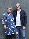 To voksne står tæt sammen foran en grå væg i afslappet tøj