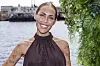 Person fra Temptation Island smiler ved vandet med grønne planter i forgrunden.