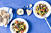Græsk salat med kikærter og fetadressing anrettet på hvide tallerkener med brød på blå dug.