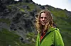 Kvinde i grøn jakke står alene i blæsende nordligt bjerglandskab.