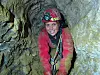 Speleolog med hjelm og pandelampe kravler i smal grottepassage