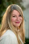 Smilende kvinde med langt lyst hår i udendørs portræt med sløret grøn baggrund.