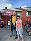 To personer står foran en rød bygning på en campingplads med cykler parkeret ved siden af.