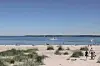Strandgæster på sandstrand med sejlbåde på roligt hav i baggrunden