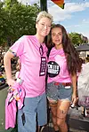To personer i pink  trøjer står på en pridevogn med regnbueflag omkring sig