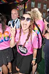 Smilende deltager i pink trøje poserer med fredstegn under farverig parade.