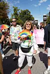 Smilende deltager holder en regnbuevifte under en farverig gadeparade.