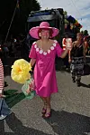 Person i pink kjole og hat går smilende foran paradevogn under Strax-optog.