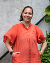Kvinde i orange bluse står foran lys betonmur med grønne planter