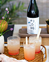 Tre lyserøde drinks med is på fletbakke foran en japansk flaske på bord