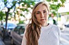 Ung blond kvinde med alvorligt udtryk står på et fortov i en by