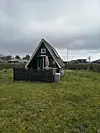 Mørkt A-formet sommerhus med terrasse og parasol på stor græsplæne