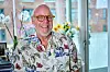 Palle Richard Laursen smiler i farverig skjorte foran vindue og blomster i stuen.