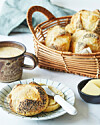 Tallerken med rundstykker, smørkniv, kaffe og kurv med brød på morgenbord