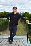 Person står afslappet op ad glasrækværk på tagterrasse med park i baggrunden