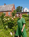 Kvinde i grøn kjole står i farverig have foran rødt murstenshus