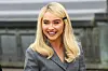 Sabrina Carpenter i grå blazer smilende foran showindgang i Paris