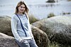 Kvinde i lys striktrøje står ved store klipper ved en søbred