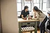 Mor og teenage­søn læner sig over køkkenbordet og taler sammen med kaffekopper foran sig.