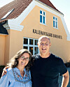 Smilende par foran den gule facade på Kallehavegaard Badehotel i solskin